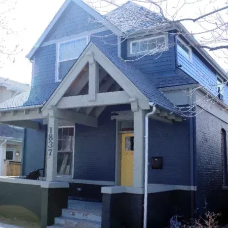 A renovated two-story blue house with a yellow door and grey gabled porch.
