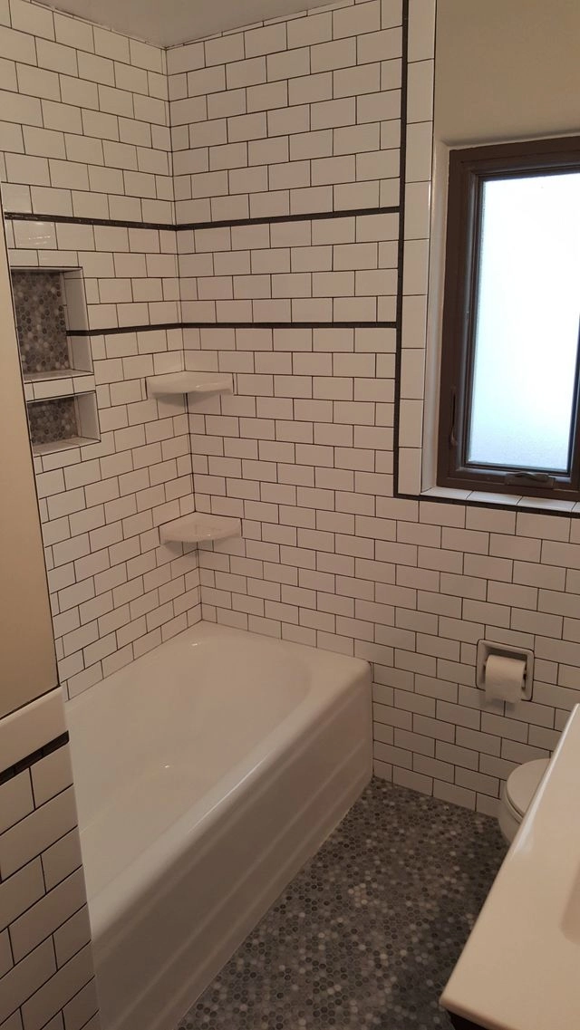 A renovated bathroom featuring white subway tile walls, a white bathtub, and grey pebble tile flooring.