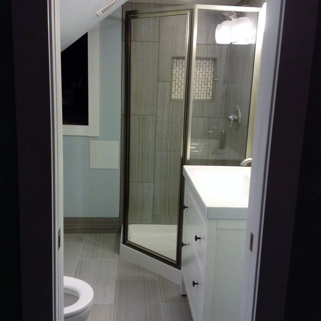 A modern bathroom featuring a glass corner shower, grey tiling, and a white vanity.