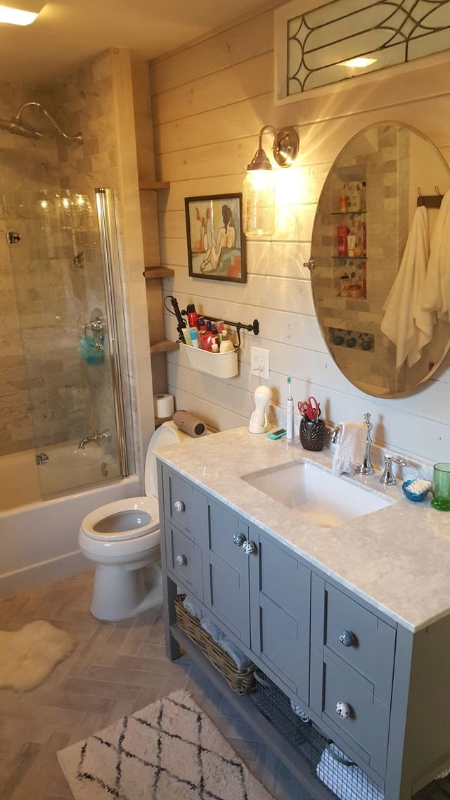 A modern rustic bathroom featuring a grey vanity, marble top, oval mirror, and shiplap walls.
